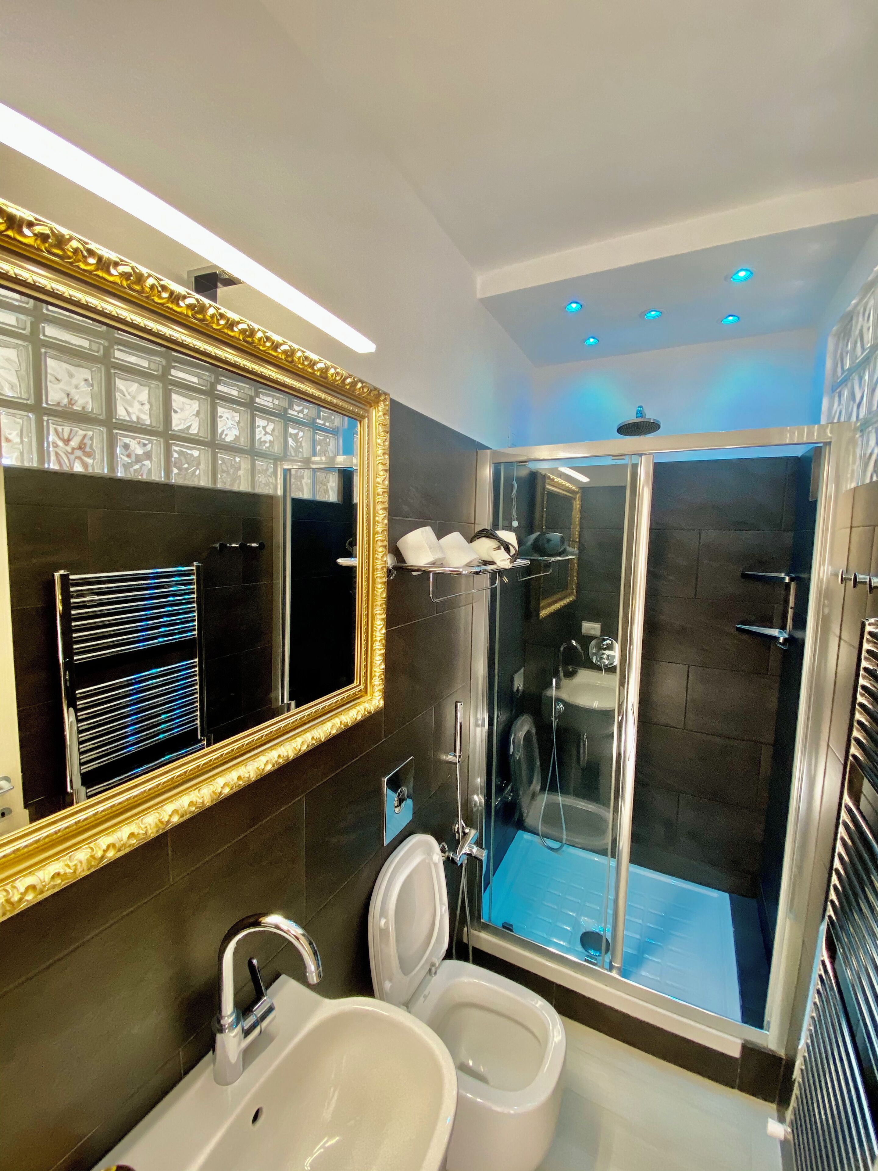 A modern bathroom with a large mirror, dual sinks, a shower enclosure, and a toilet.