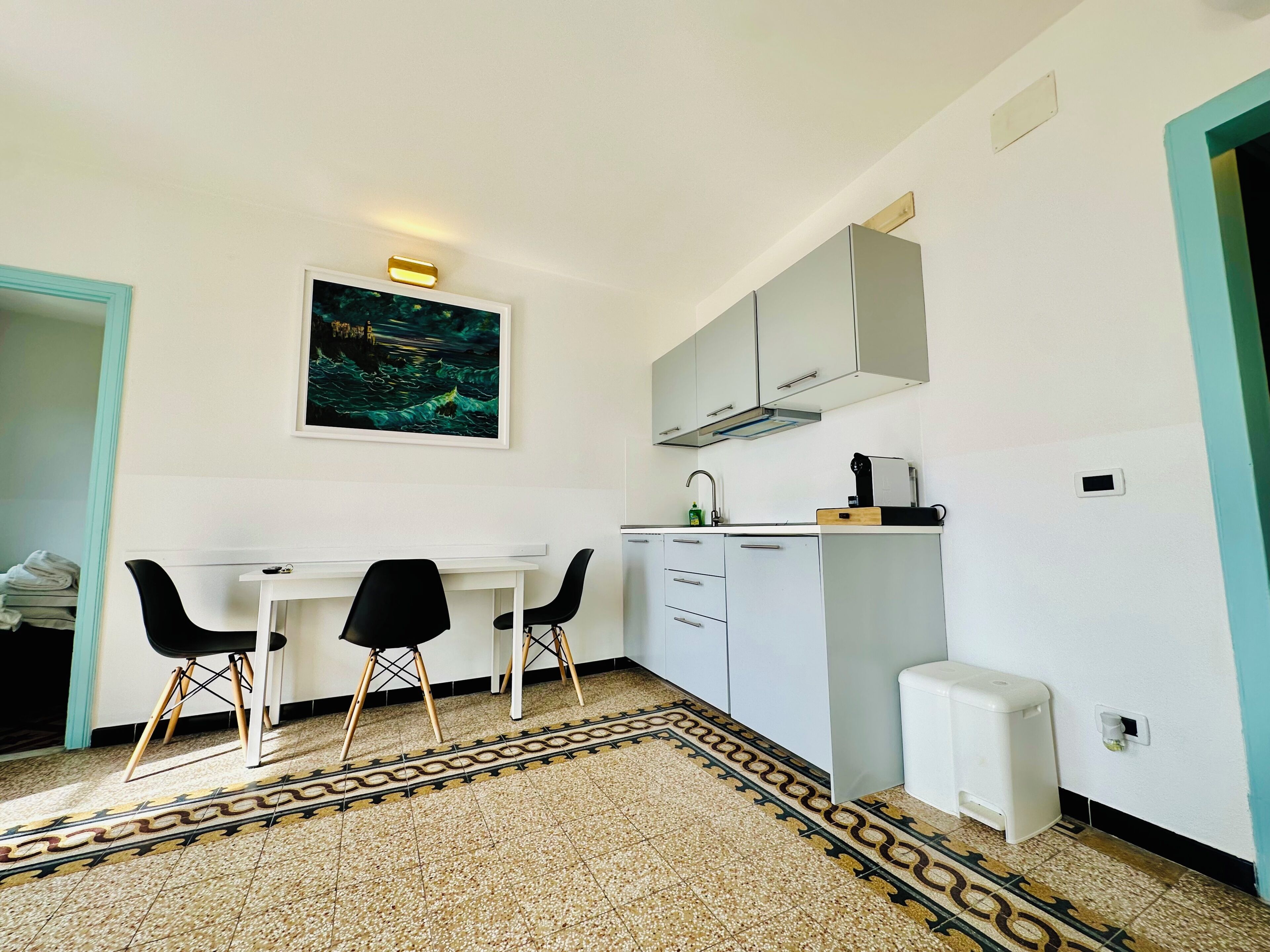 A compact kitchen with a dining area, a painting on the wall, and a patterned floor.