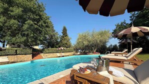 Area piscina con sedie a sdraio, un tavolo con cibo e bevande e una piscina cristallina blu.