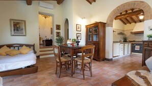 Une pièce confortable comprenant un lit, une table à manger, des chaises, un coin cuisine avec une arche et un escalier menant à une autre pièce.