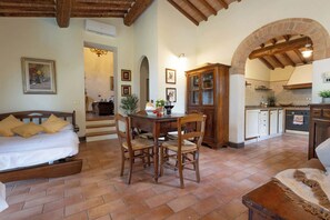 A cozy room with a bed, a dining table, chairs, a kitchen area with an archway, and a staircase leading to another room. - Spacious Apartment Villa in Tuscan Vineyard Estate (Poggibonsi)