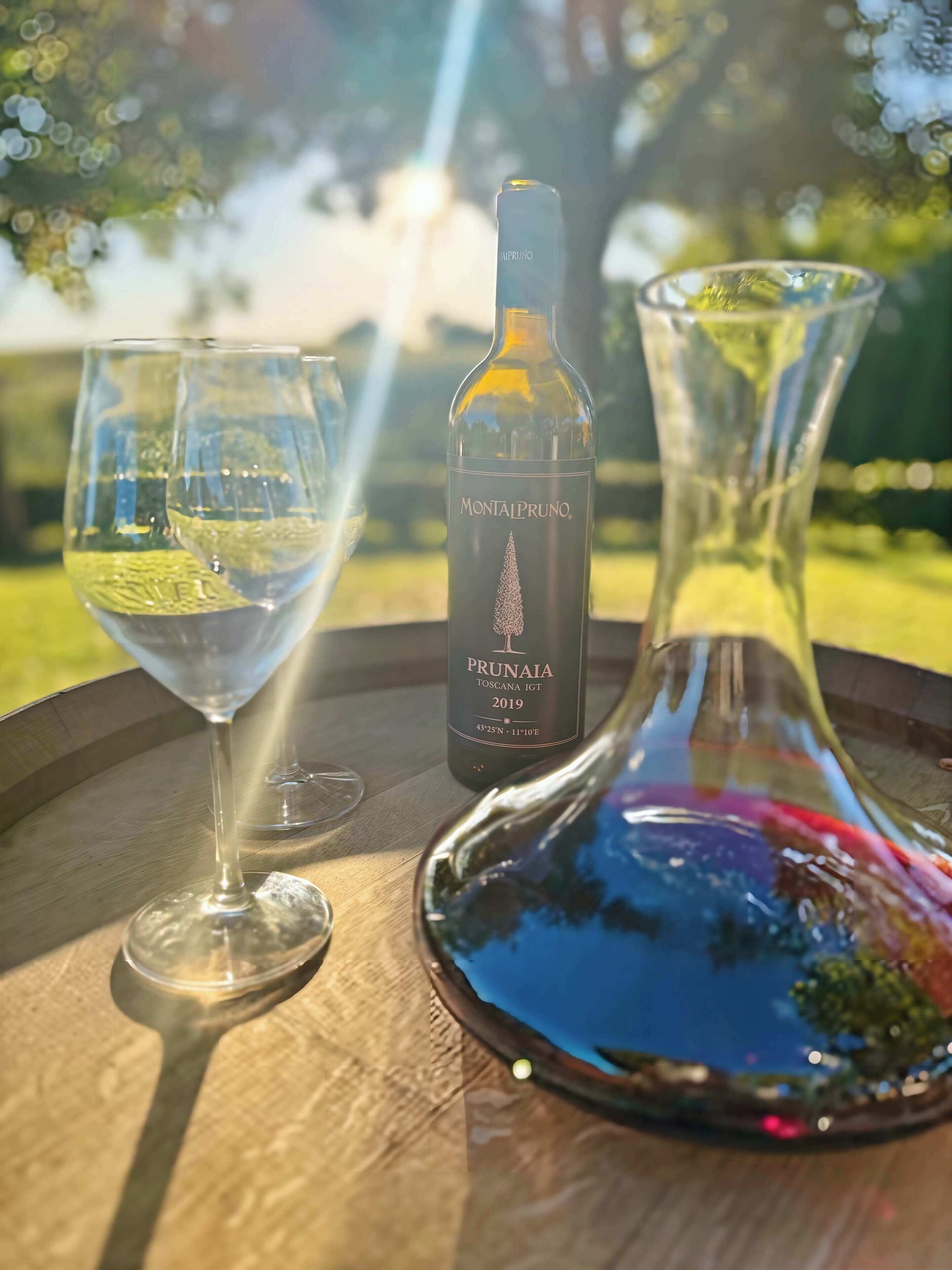 A bottle of Montalpruno Prunaia wine, a glass of white wine, and a decanter on a wooden tray.