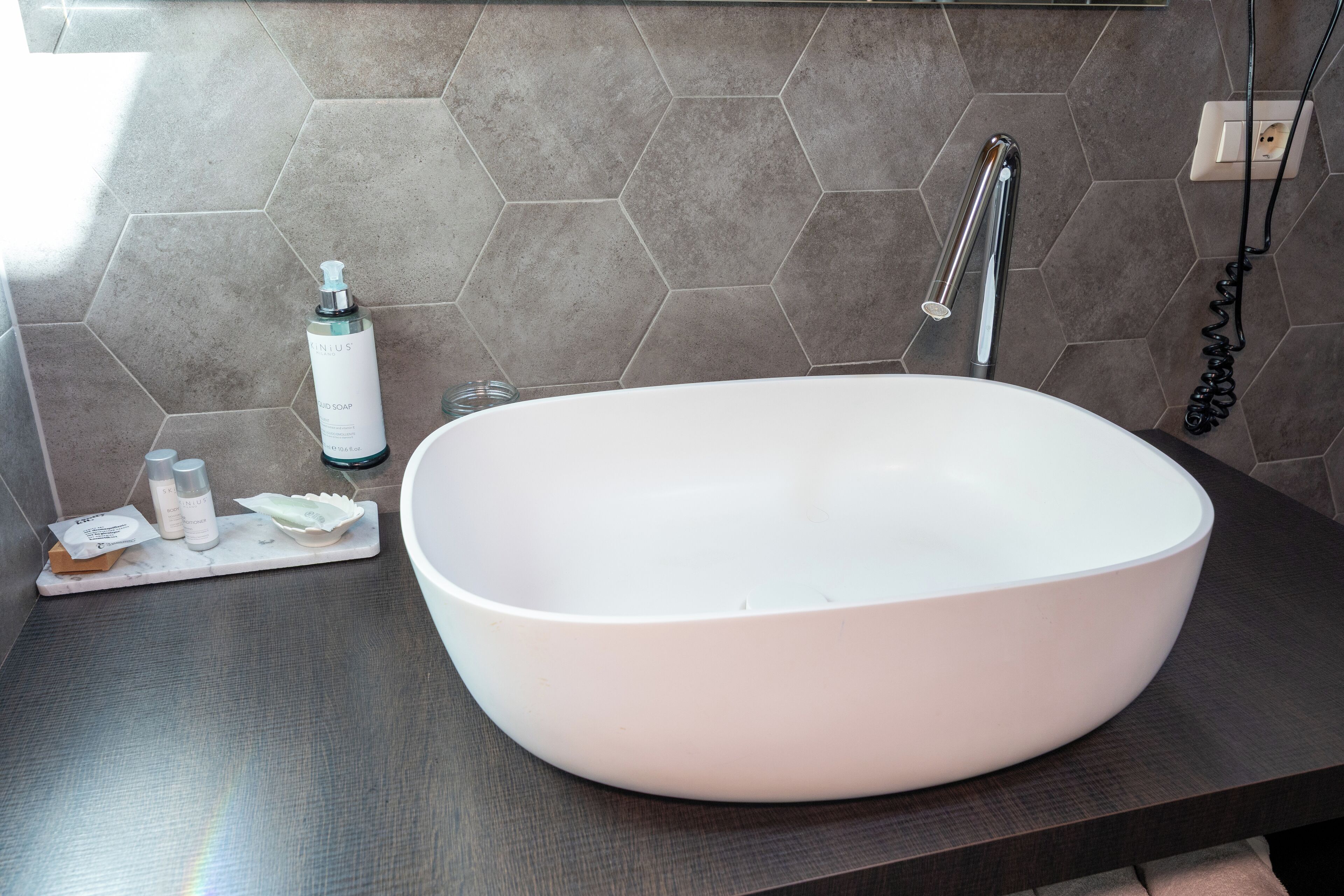 Une salle de bain moderne avec un grand lavabo sur pied blanc, un plan de travail foncé et un pare-feu en carreaux hexagonaux.
