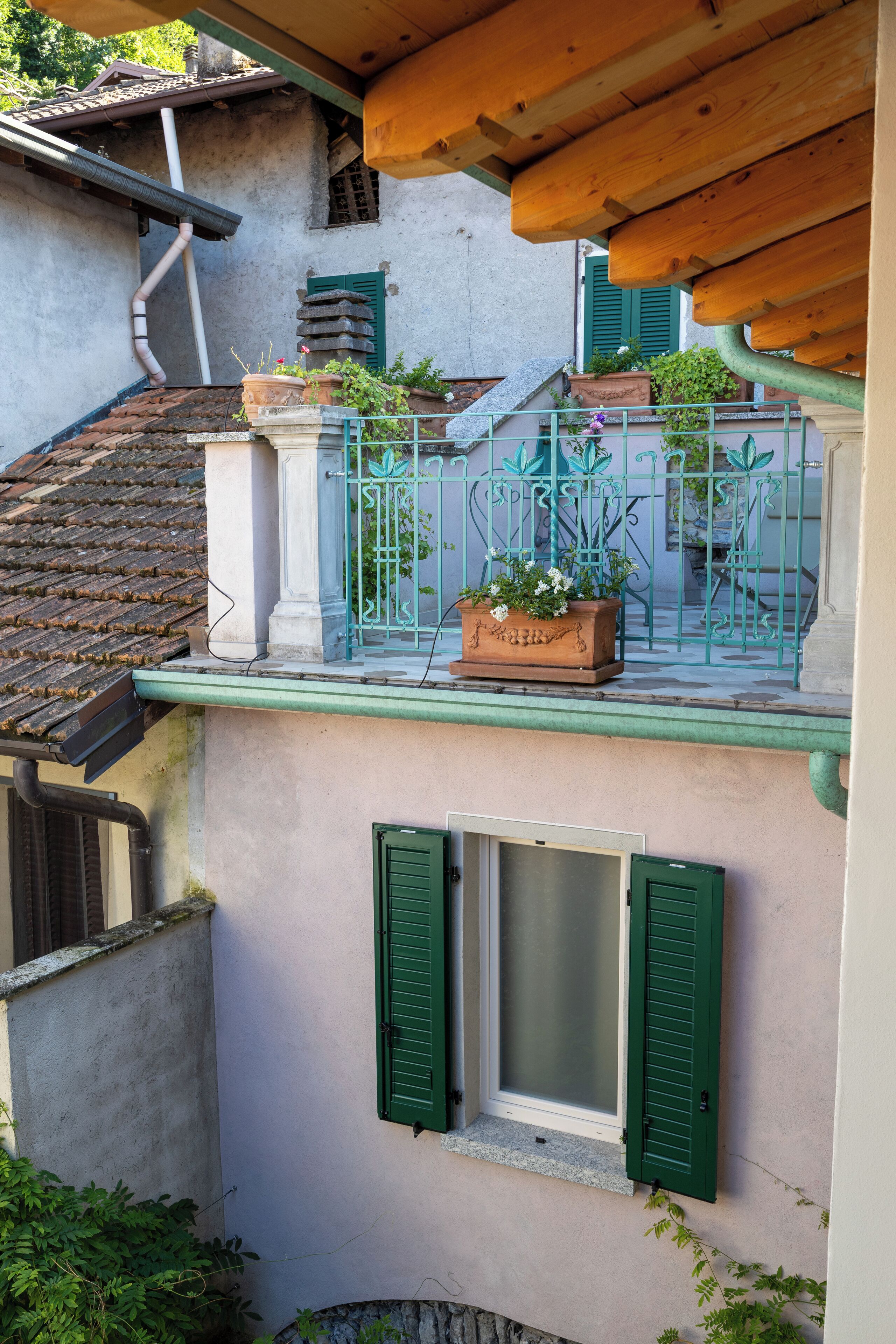 Um edifício com varanda, venezianas verdes e plantas em vasos.