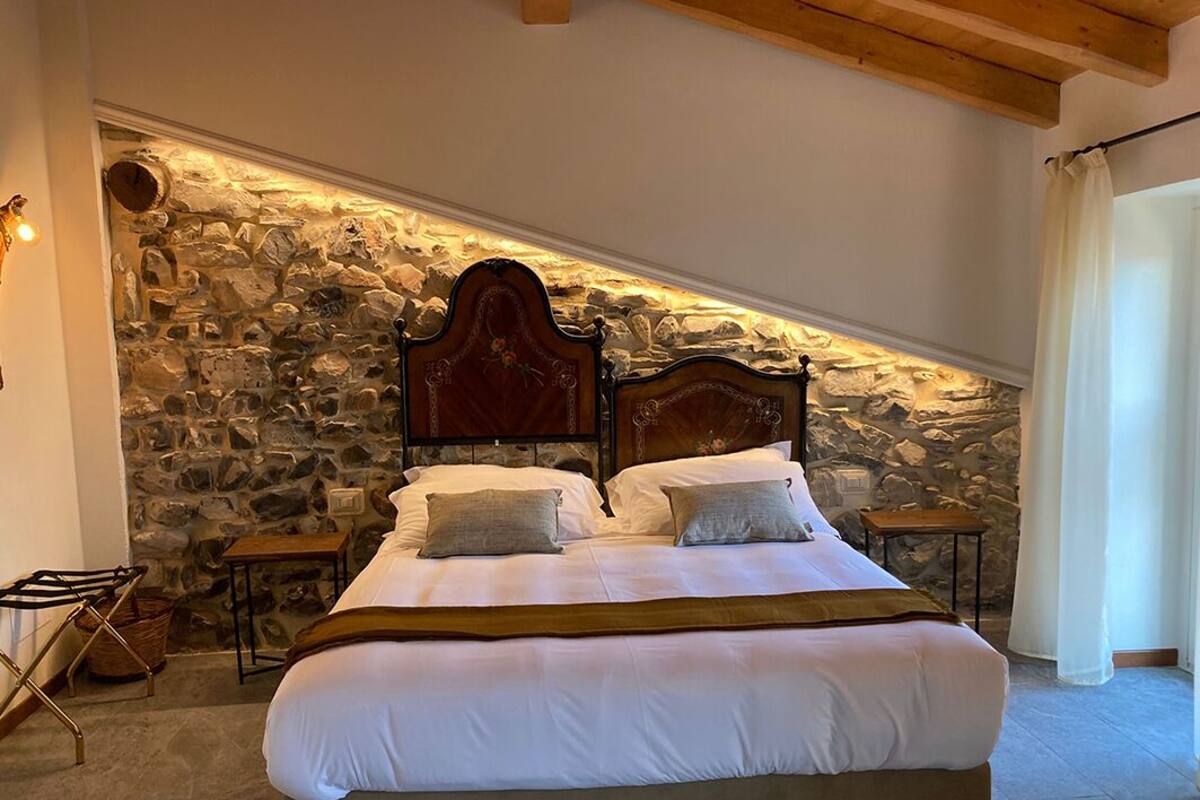A bedroom with a stone wall, a wooden bed frame, and a sloped ceiling.