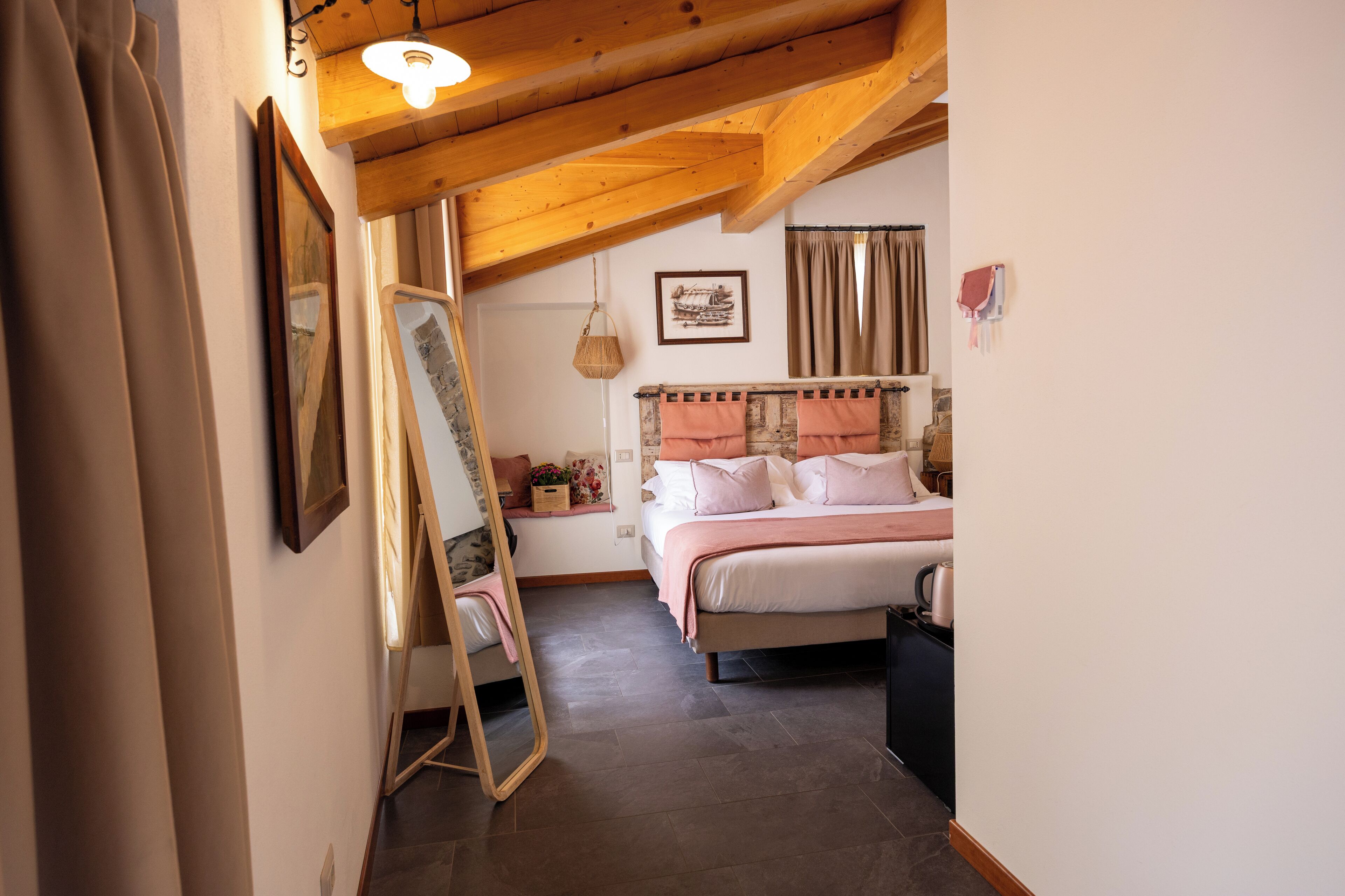 Habitació amb un llit, un mirall, una làmpada penjant i una finestra amb cortines.