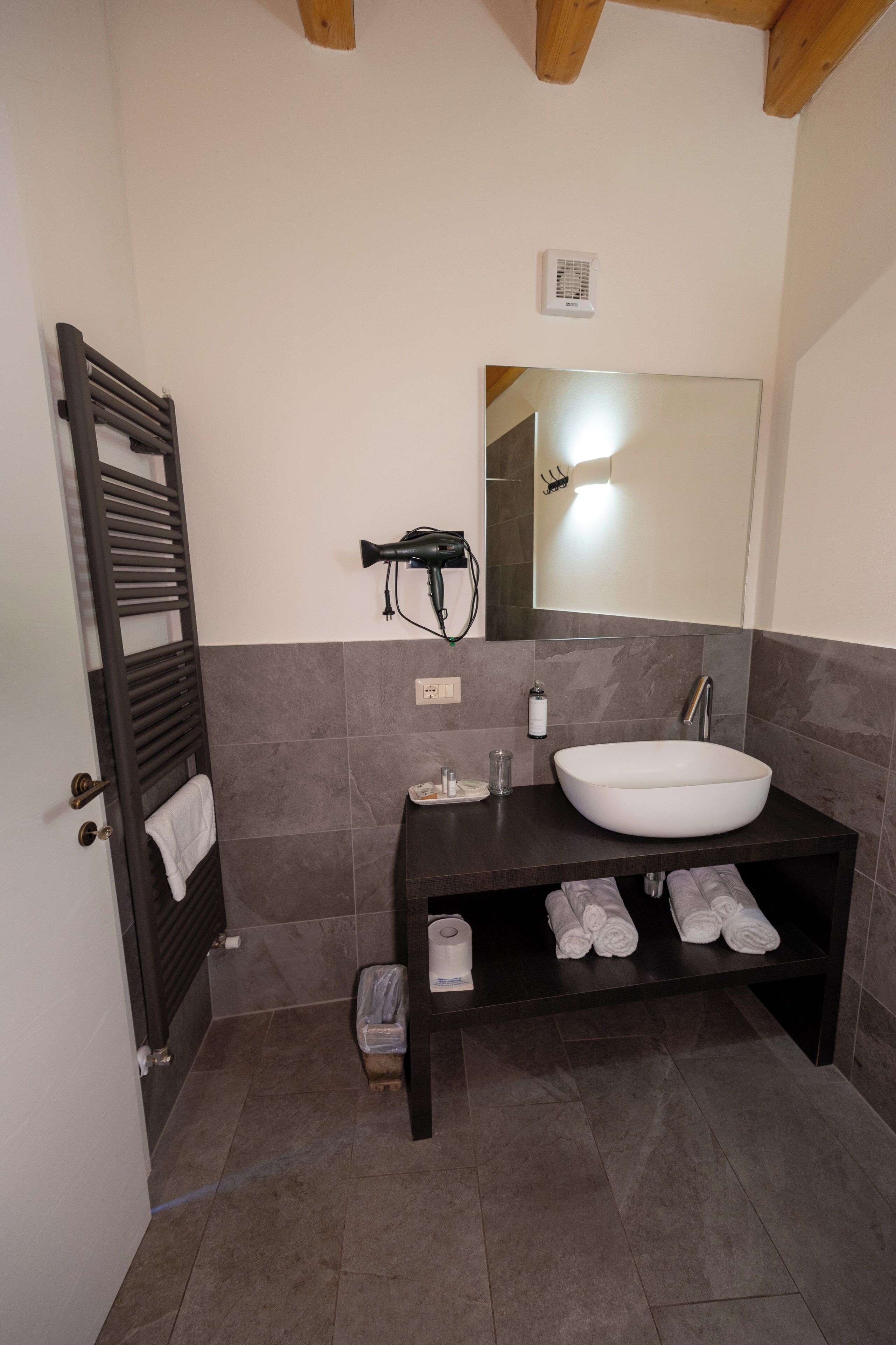 Un baño con un lavamanos grande de color blanco, tocador de madera oscura y un perchero para toallas.