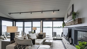 A modern living room with a large window, a sofa set, a fireplace, and a view of the water.
