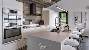 Une cuisine moderne équipée d’appareils électroménagers Bosch, dotée d’un grand îlot central, de tabourets de bar et offrant une vue sur la verdure.