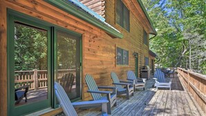 En stuga byggd av trä med en veranda, utomhusmöbler och utsikt över den omgivande skogen.