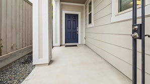 A narrow, covered walkway leading to a dark blue door with a metal handle, flanked by light-colored siding and a wooden fence. - Best Location near Downtown/The Heights (Houston)