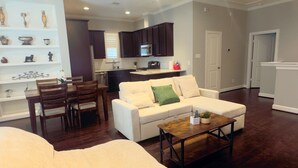 A modern living room with a white sofa, a wooden coffee table, and a dining area with a wooden table and chairs. - Best Location near Downtown/The Heights (Houston)