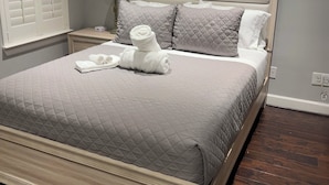 A neatly made bed with a quilted grey bedspread, two pillows, and rolled white towels. - Best Location near Downtown/The Heights (Houston)