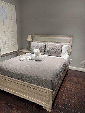 Un lit bien fait, recouvert d’une courtepointe grise matelassée, avec deux oreillers et des serviettes blanches pliées.
