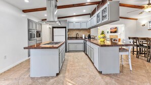 A modern kitchen with grey cabinets, a central island, and a dining area with wooden chairs.