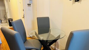 Ein Raum mit einem Glastisch, der von vier blauen Stühlen umgeben ist, Holzboden und einer weißen Tür mit Lichtschalter.