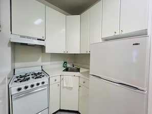 Una cucina con mobili bianchi, un fornello, un lavello e un frigorifero.