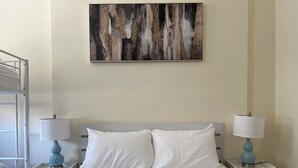 Ein Hotelzimmer mit einem Bett, zwei Nachttischen mit Lampen, einem Etagenbett und einem an der Wand hängenden abstrakten Gemälde.