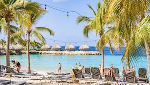 Une plage avec des chaises longues, des palmiers et des parasols en feuilles de palmier.