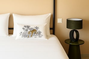 A bed with white bedding, a tiger-themed pillow, and a modern lamp on a side table. - 2 bedroom apt @bluebay golf resort with pool. 5 min walk from bluebay beach (Willemstad)