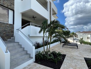 A modern multi-story house with a staircase leading to a balcony, surrounded by landscaped gardens and palm trees. - 2 bedroom apt @bluebay golf resort with pool. 5 min walk from bluebay beach (Willemstad)