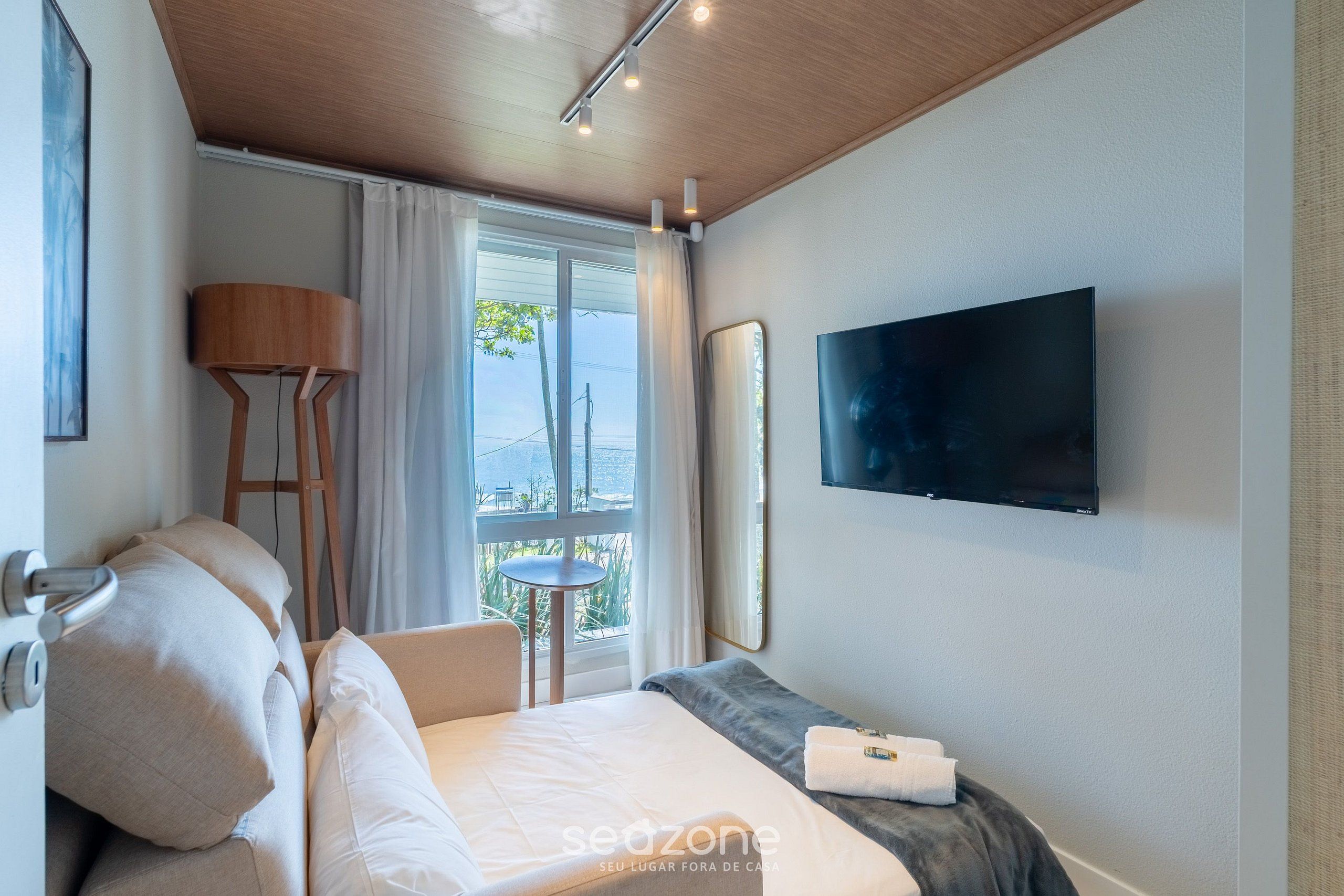 Una habitación de hotel con cama, televisión, ventana con cortinas y vistas al exterior.