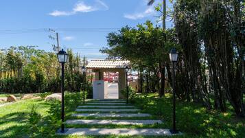 Un camino que lleva a un edificio con techo de tejas, rodeado de abundante vegetación y dos farolas.