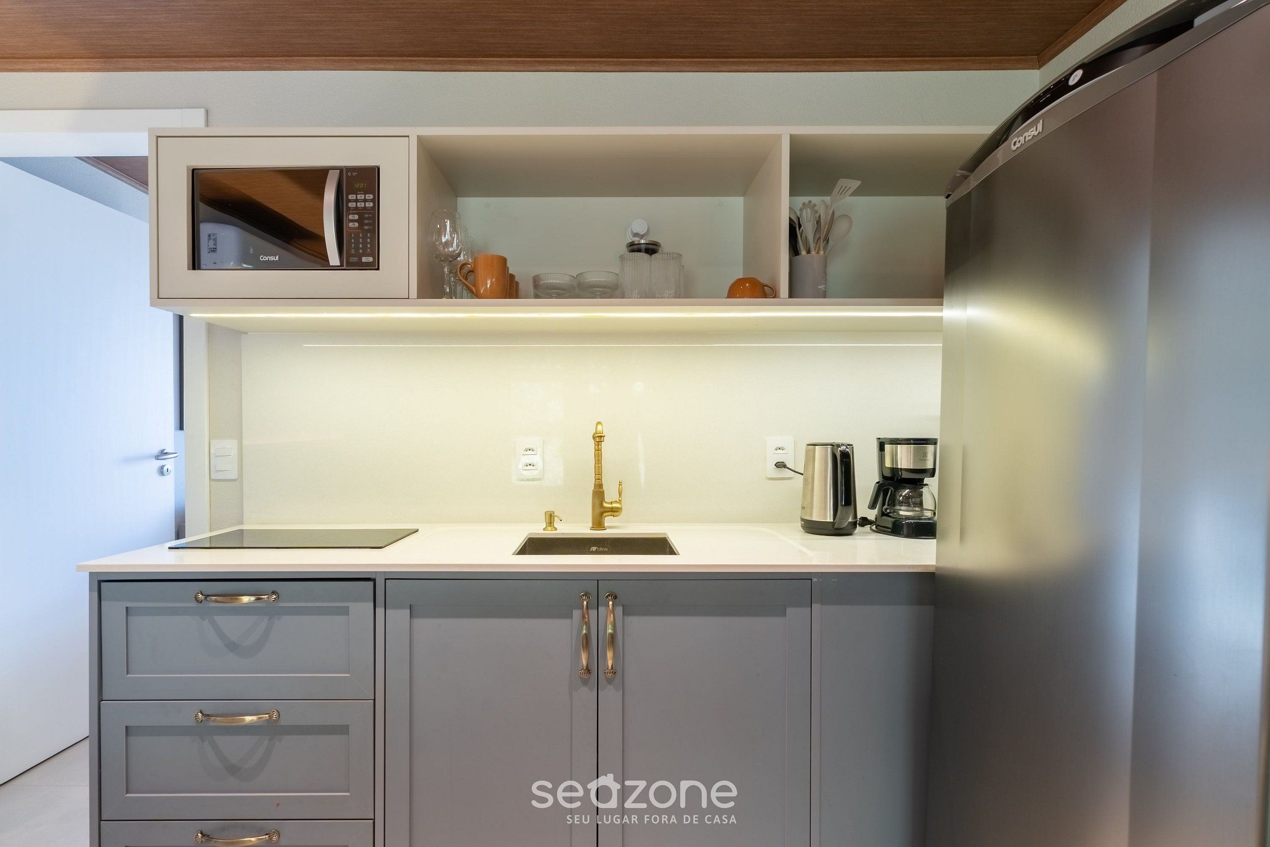 Una cocina moderna con armarios grises, un refrigerador de acero inoxidable, un microondas y una cafetera.