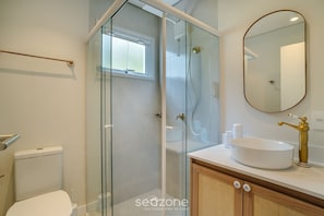 A bathroom with a glass shower enclosure, a white sink with a gold faucet, and a mirror on the wall. - Beachfront Condominium in Morro das Pedras - Ftss (Florianópolis)