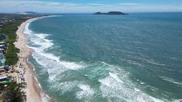 Une vue aérienne d’une plage avec une longue étendue de sable, des vagues et une île au loin.