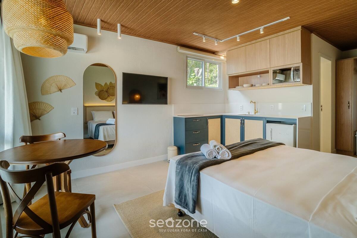 A modern bedroom with a bed, a desk, and a chair. There is a window, a mirror, and a shelf with items.