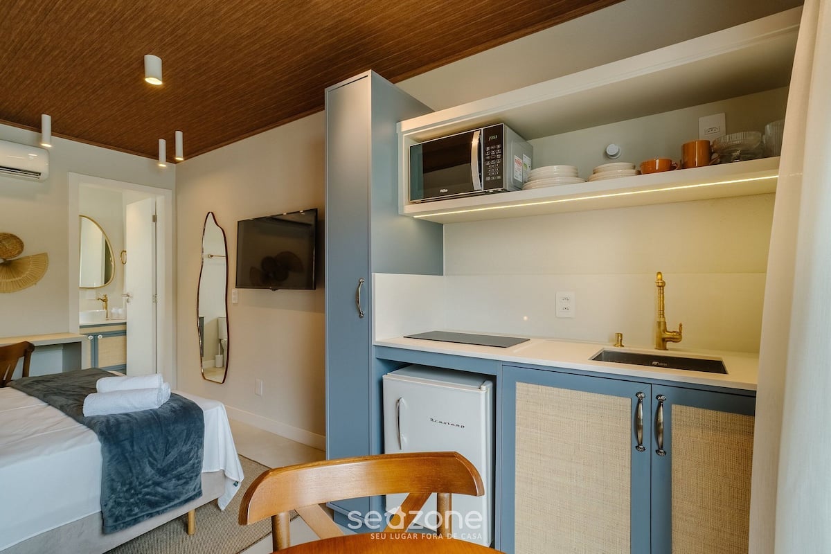 A compact hotel room with a bed, a desk, a microwave, a small refrigerator, and a sink.