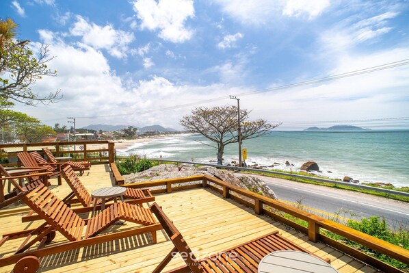 Una terraza de madera con sillones y mesas, con vistas a la playa y el océano.