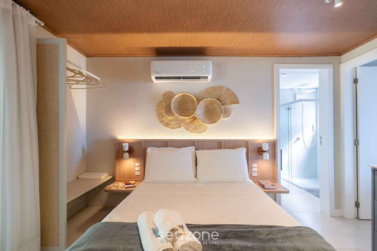 A modern hotel room with a large bed, a wall-mounted air conditioner, and a decorative wall piece.