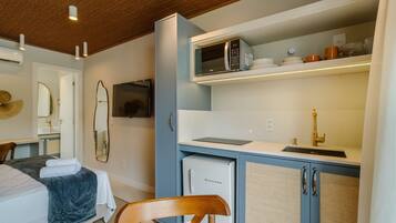 A compact hotel room with a bed, a desk, a microwave, a small refrigerator, and a sink.