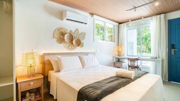 A well-lit bedroom with a bed, bedside table, lamp, and a view of greenery outside.
