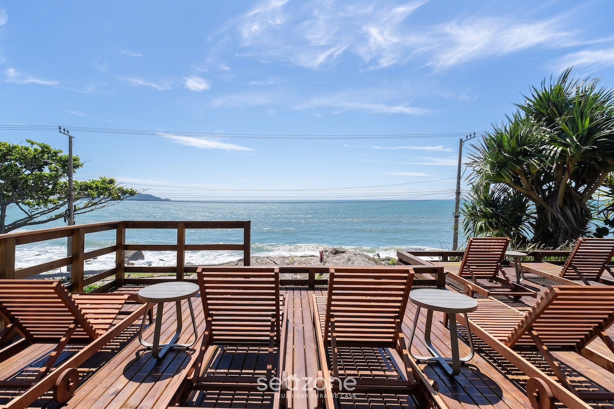 Una terraza de madera con sillones y mesas con vista a una playa y olas.
