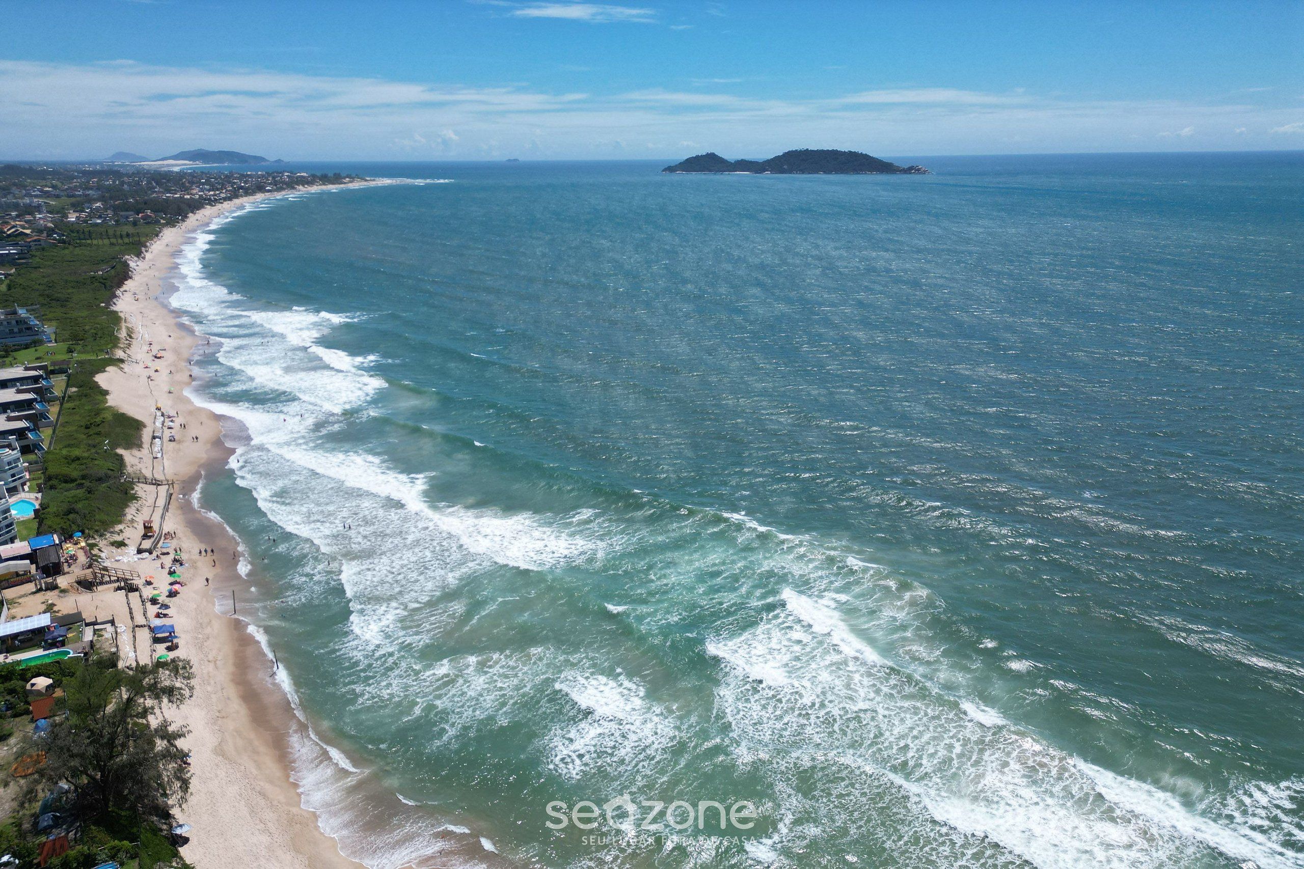 An aerial view of a beach with a long stretch of sand, waves, and a distant island.