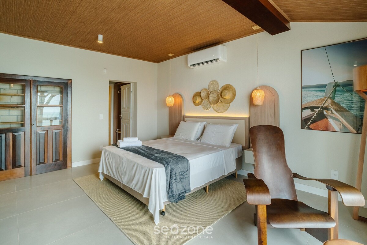 A bedroom with a bed, a wooden chair, a wall-mounted air conditioner, and a framed picture of a boat.