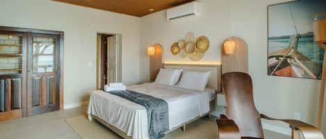 A bedroom with a bed, a wooden chair, a wall-mounted air conditioner, and a framed picture of a boat.