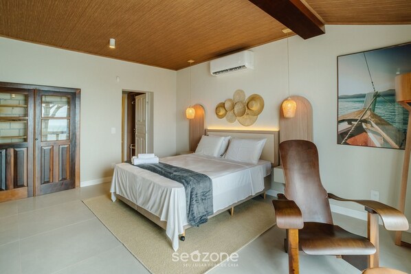 A bedroom with a bed, a wooden chair, a wall-mounted air conditioner, and a framed picture of a boat. - Beachfront Condominium in Morro das Pedras - Ftss (Florianópolis)