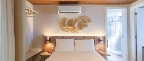 A modern hotel room with a large bed, a wall-mounted air conditioner, and a decorative wall piece.