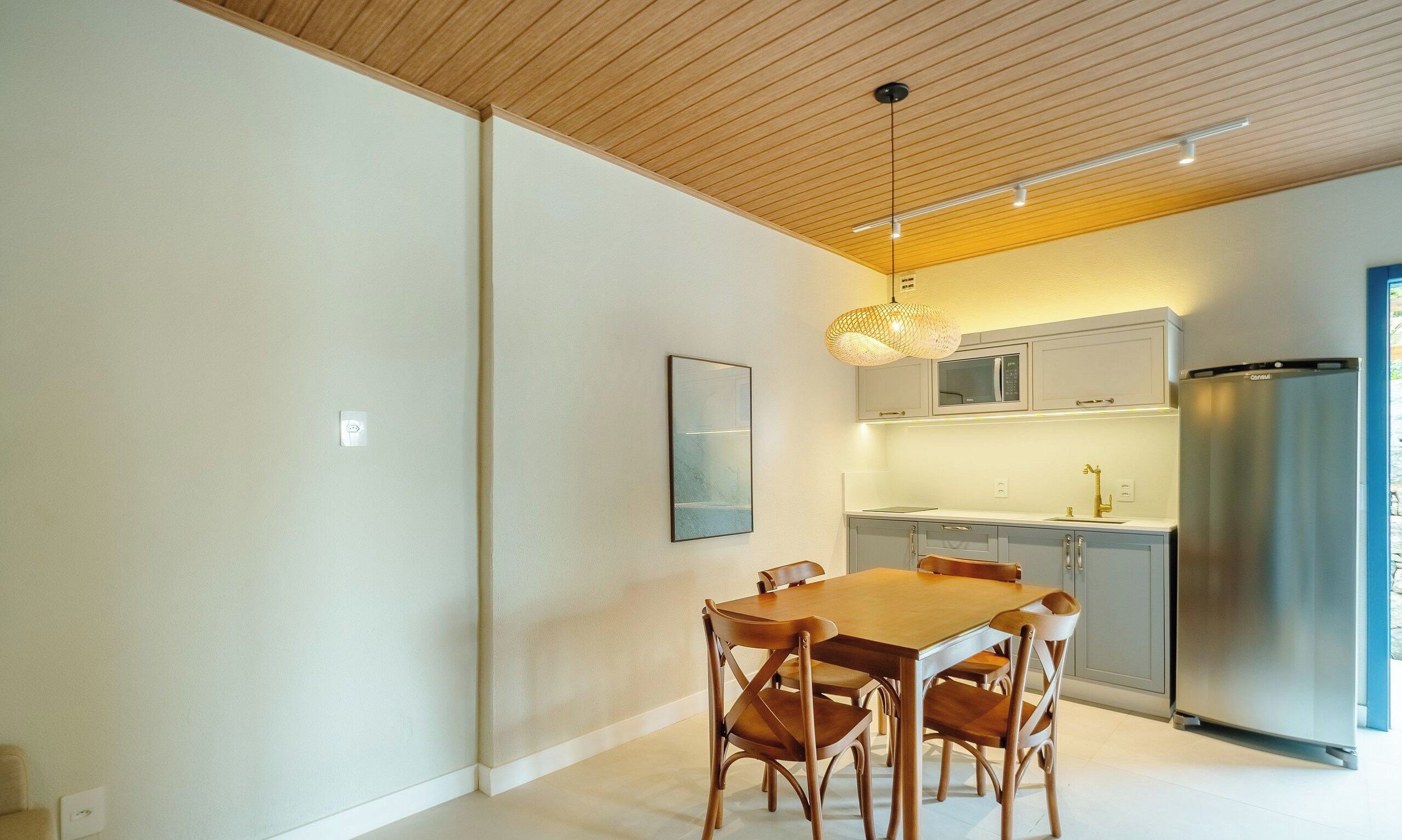 Una cocina moderna con comedor, que presenta techo de madera, paredes blancas y un refrigerador de acero inoxidable.