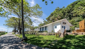 A white building with blue accents, surrounded by lush greenery and a gravel path leading to it. - Beachfront Condominium in Morro das Pedras - Ftss (Florianópolis)