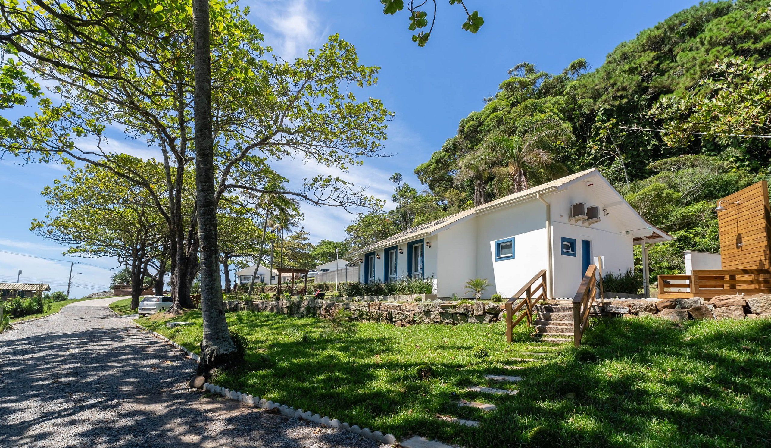 A white building with blue accents, surrounded by lush greenery and a gravel path leading to it.