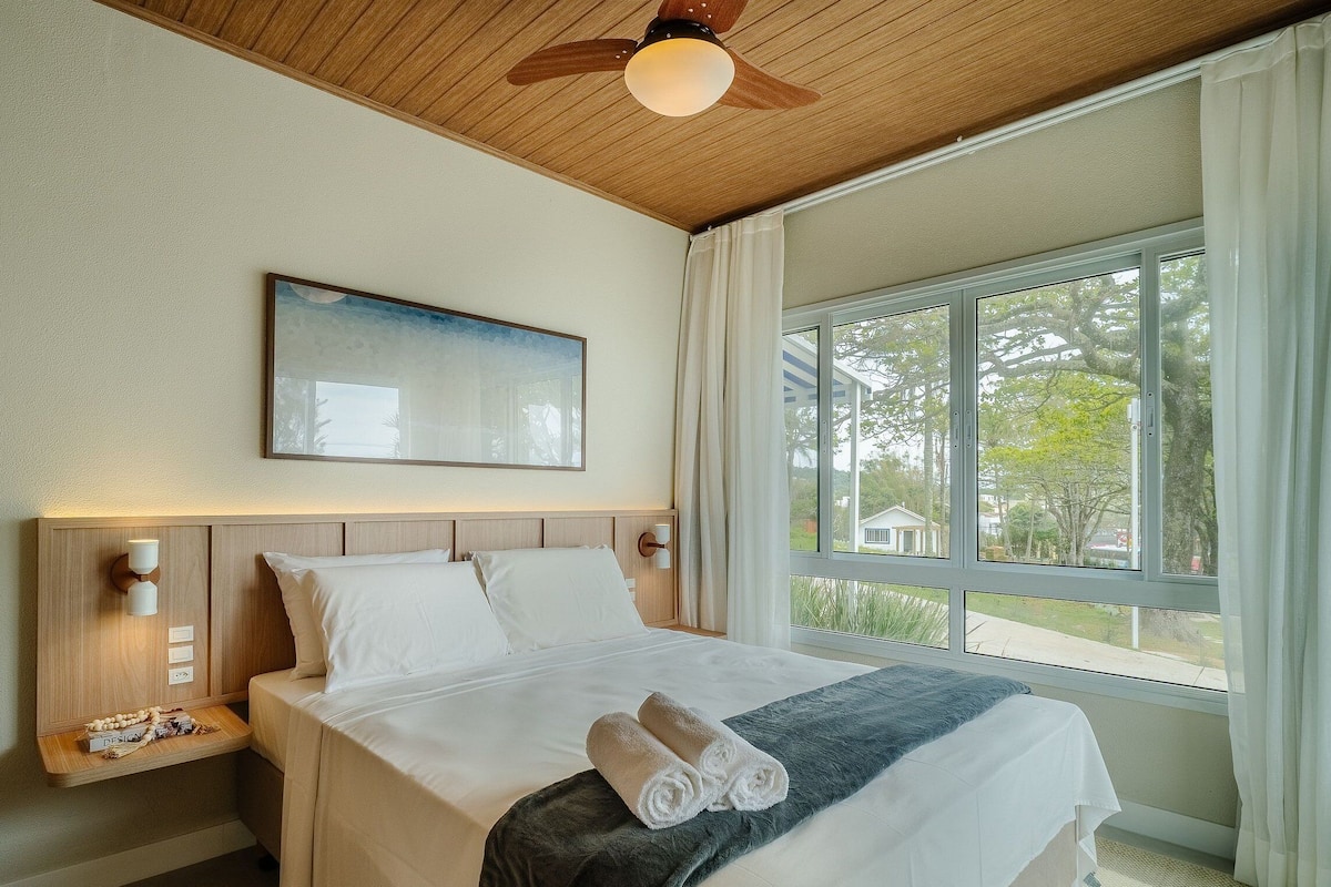 A hotel room with a bed, a ceiling fan, a window with curtains, and a wall-mounted light fixture.