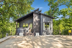 A modern building with a metal roof, large windows, and a paved entrance area. - Above the Trees | Hot Tub & On MTB Trail (Bentonville)