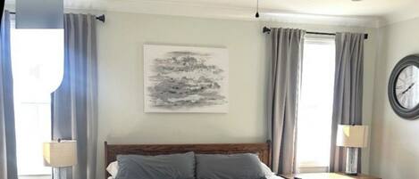 A bedroom with a wooden bed, a ceiling fan, a bedside table, a lamp, a clock, and a window with curtains.