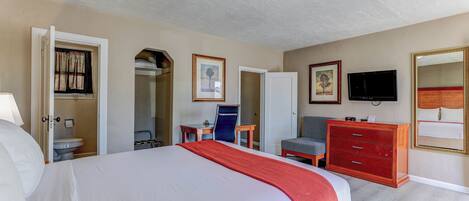 A hotel room with a bed, a desk, a chair, a dresser, a television, and a bathroom.