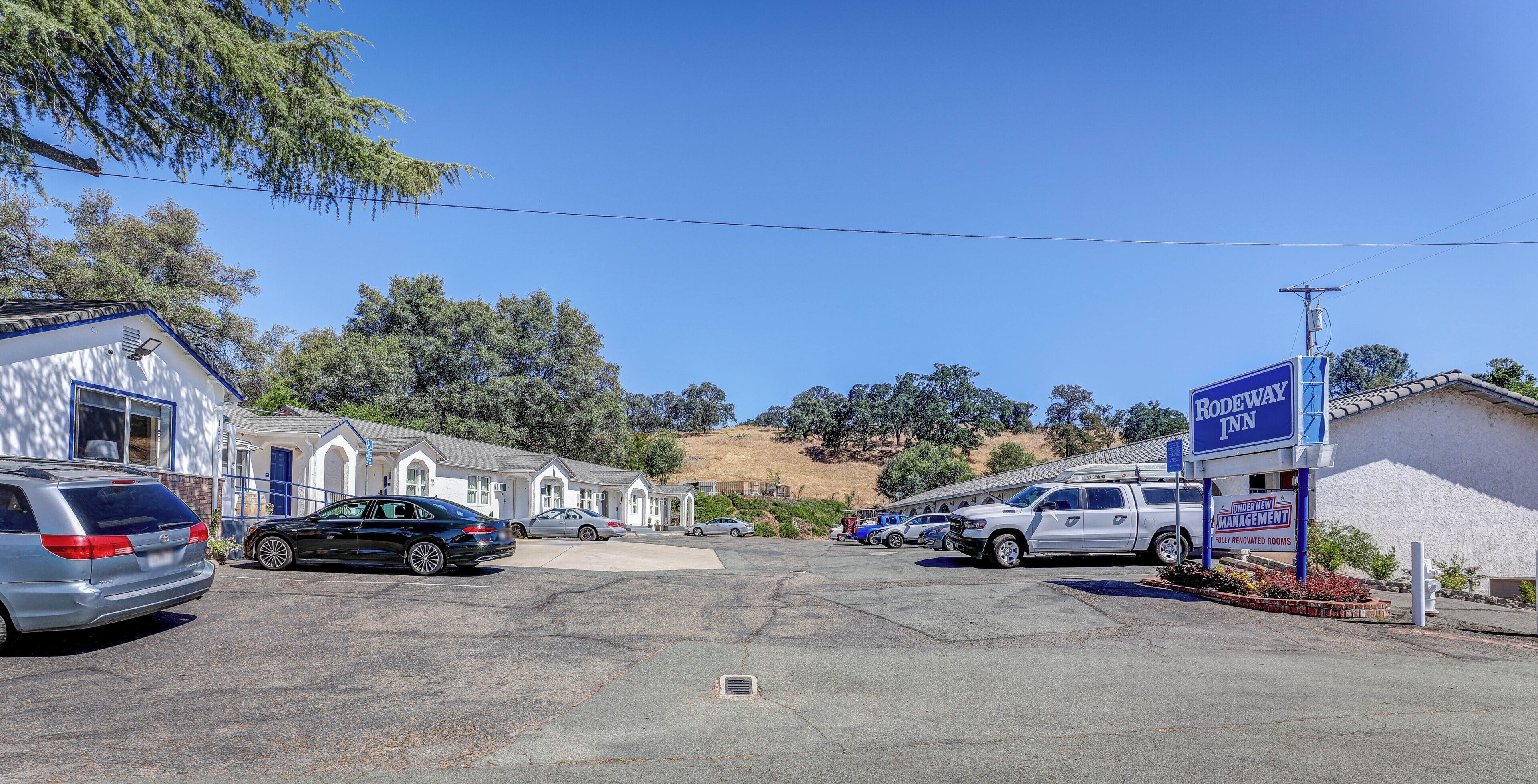 A parking lot with several cars, a motel with a sign reading 'RODEWAY INN,' and a building with a blue sign.